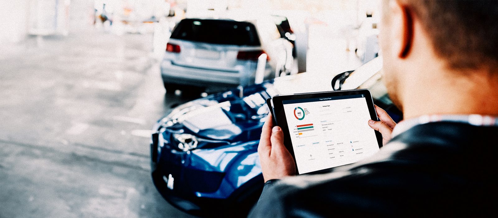 DRS SKYのタブレット画面を確認する技術者と雹害修理中の車両